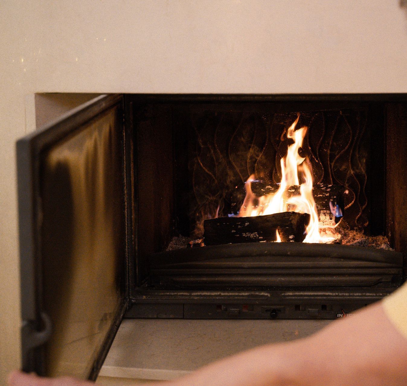 A man in a yellow shirt tends to the burning fire in a cozy indoor fireplace.
