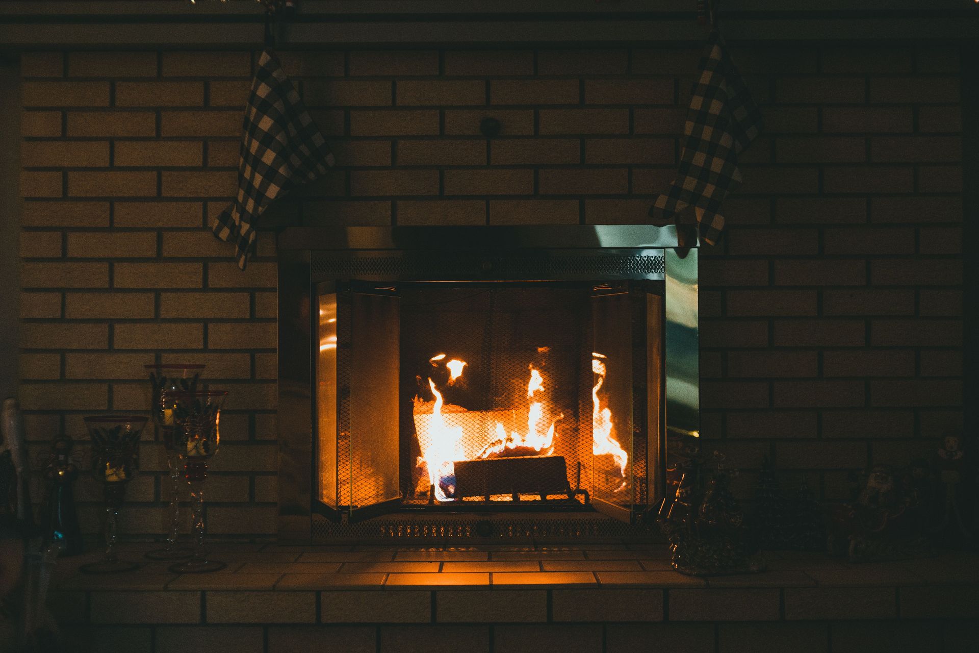 Fireplace with shiny flaming fire between retro glass candle holders and statuettes against brick wall in house